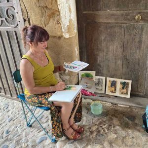Stage peinture 2023 04 14 avec une apprenante peignant à l’aqauarelle sous un porche de la manufacture royale de Villeneuvette